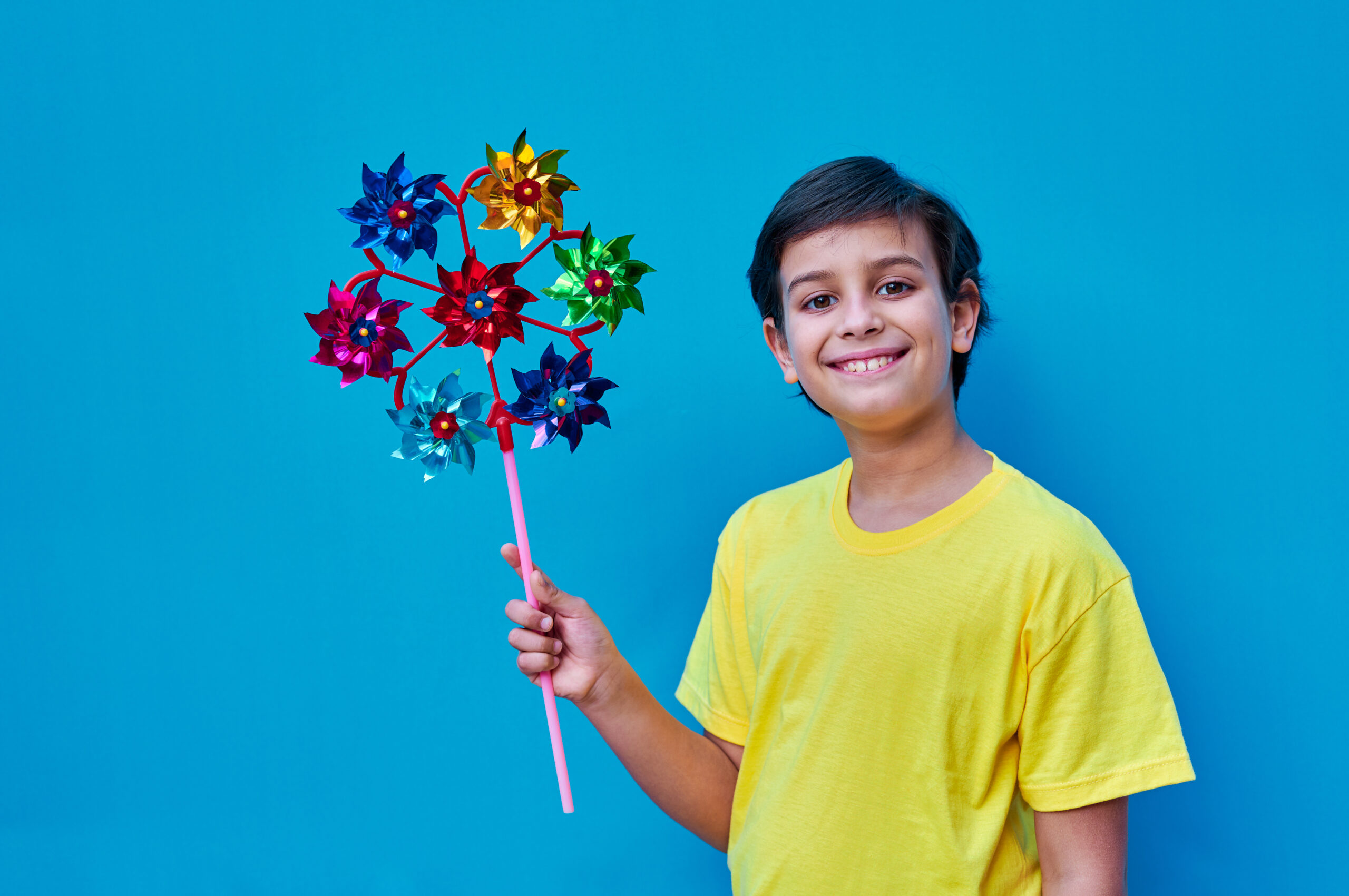 A smiling child holding a colorful pinwheel against a blue sky