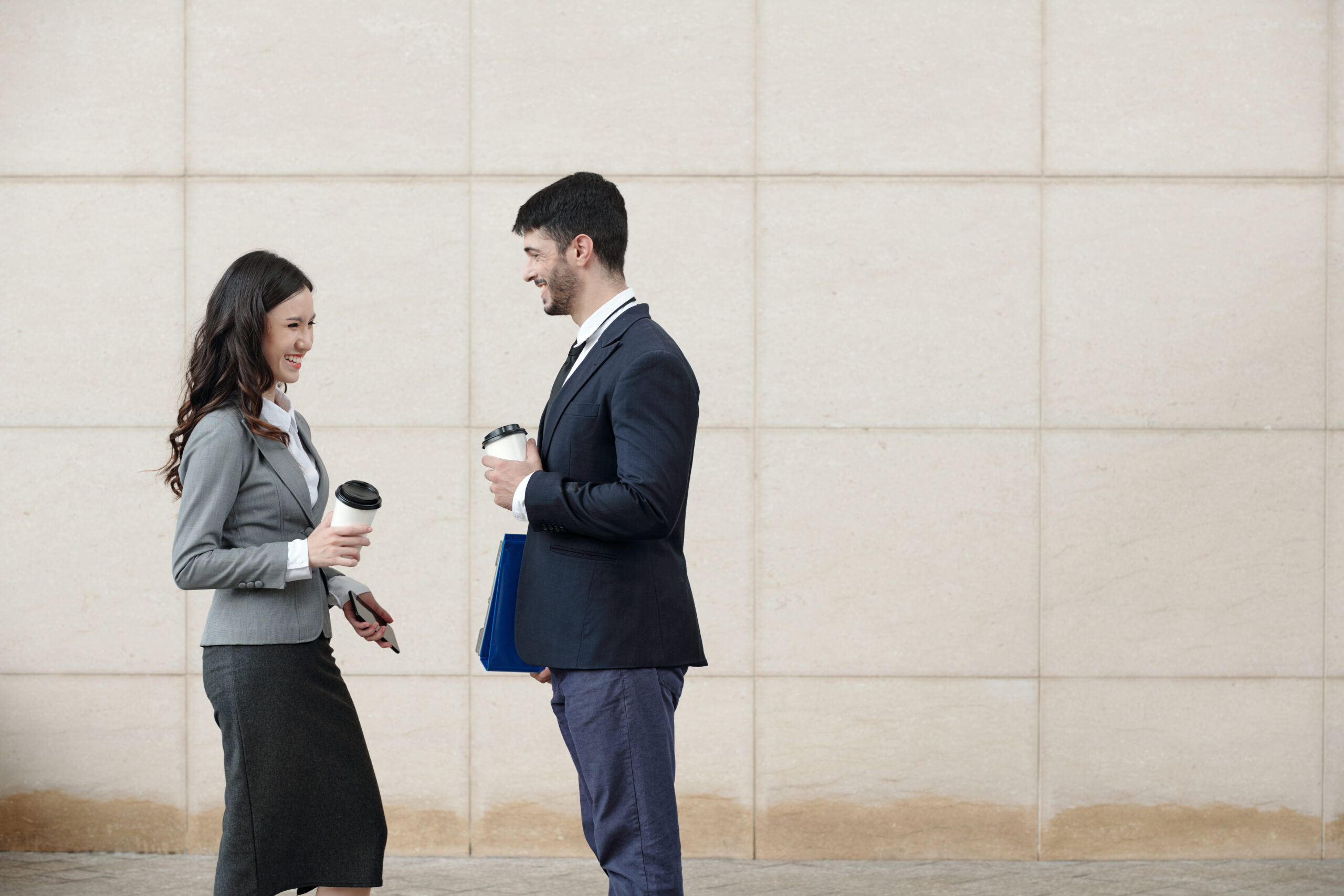 Two colleagues chatting over coffee outside an office.