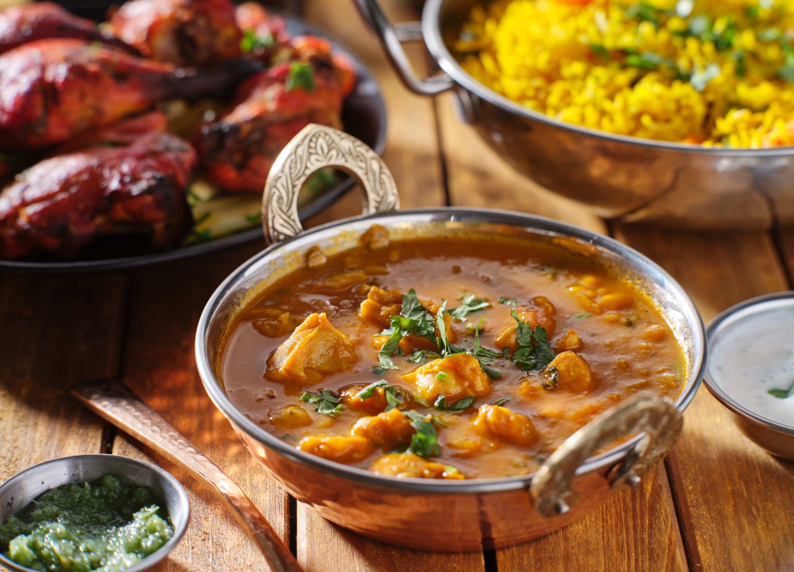 Chicken curry with rice and small dishes on a wooden table.