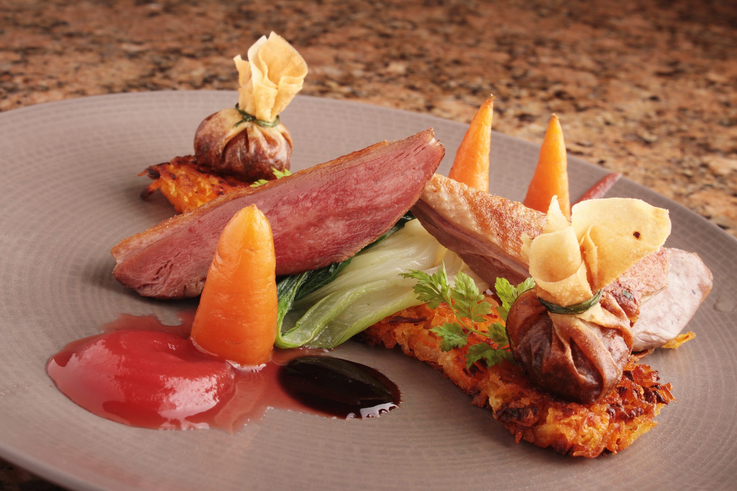 A plated duck dish with carrots and hash browns.
