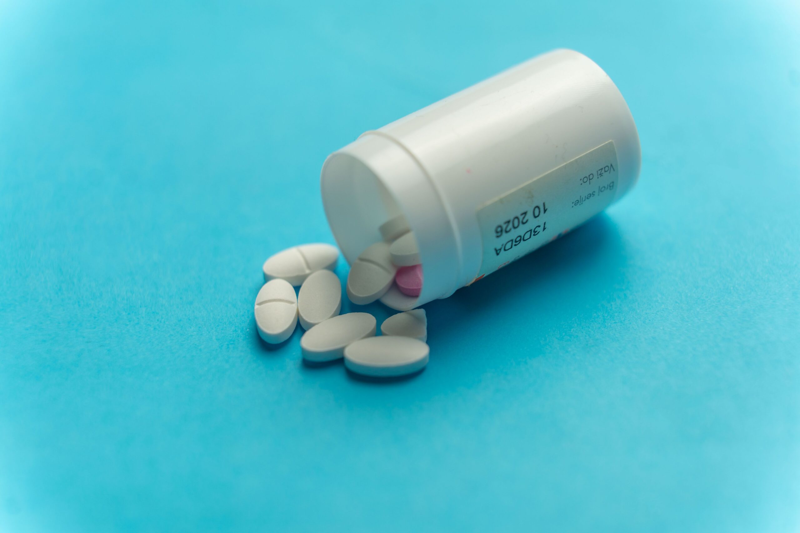 White tablets scattered on a teal surface beside an open container.