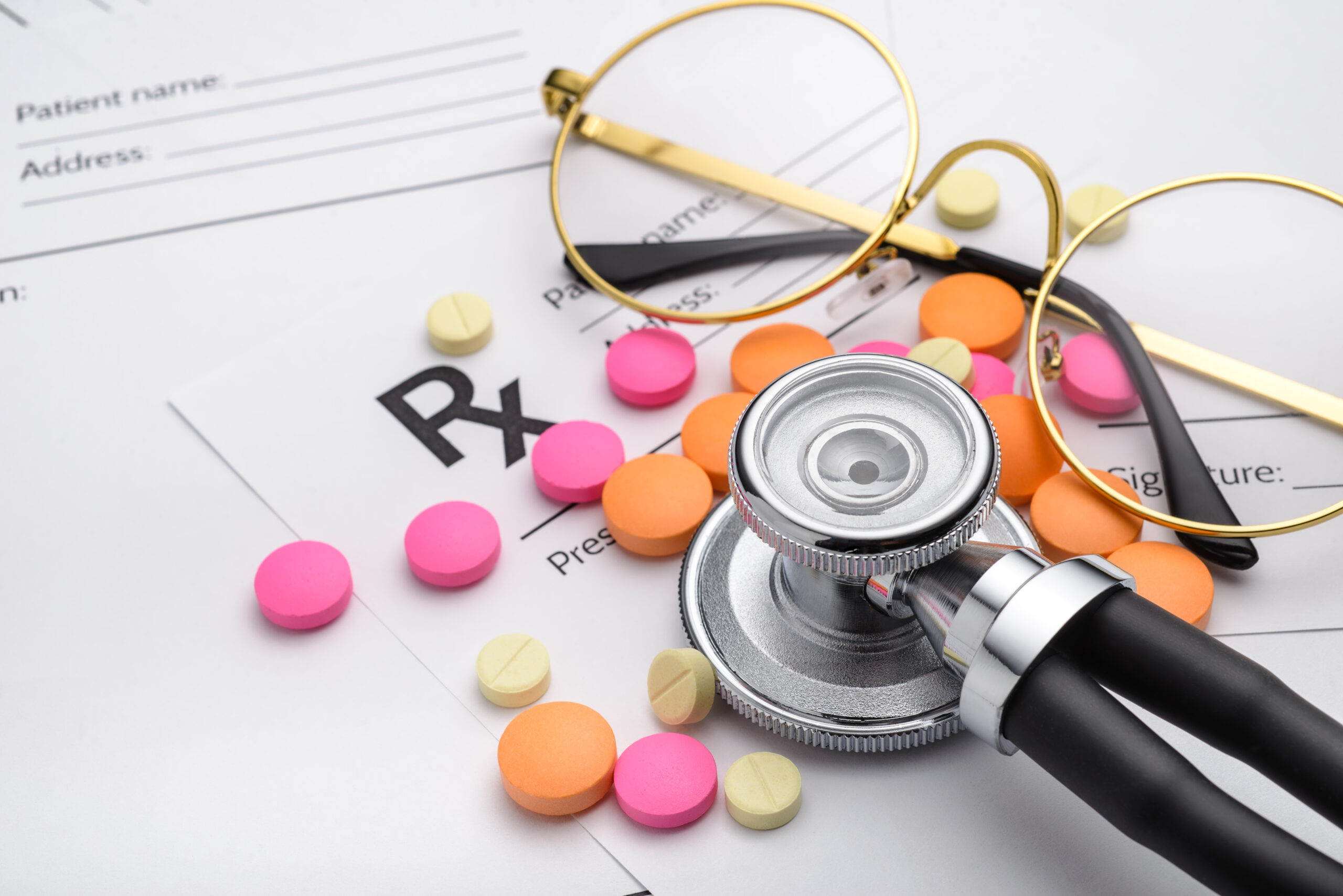 A prescription pad, stethoscope, eyeglasses, and medication on a desk.