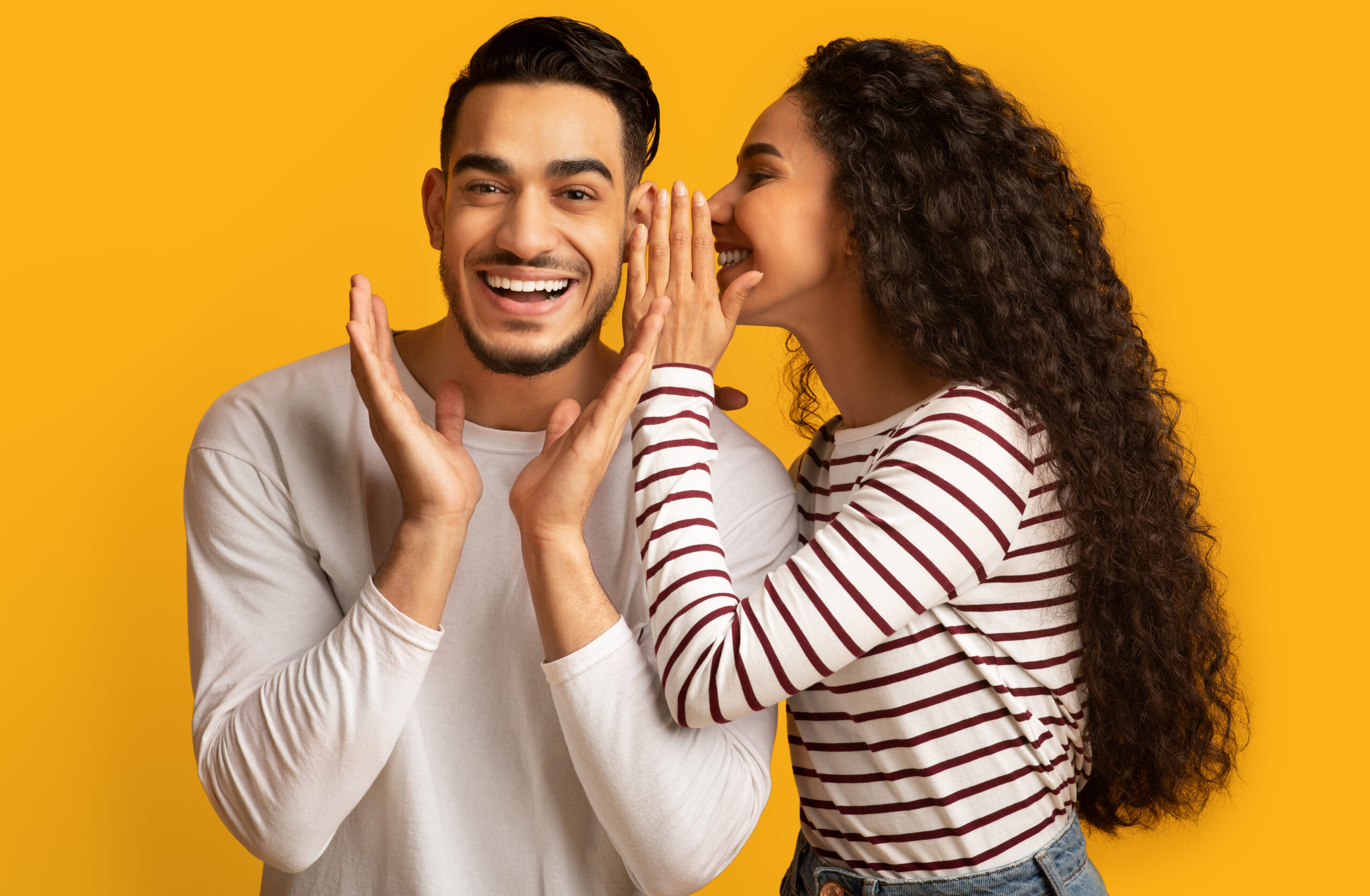 A smiling man and woman leaning in, sharing something between them.