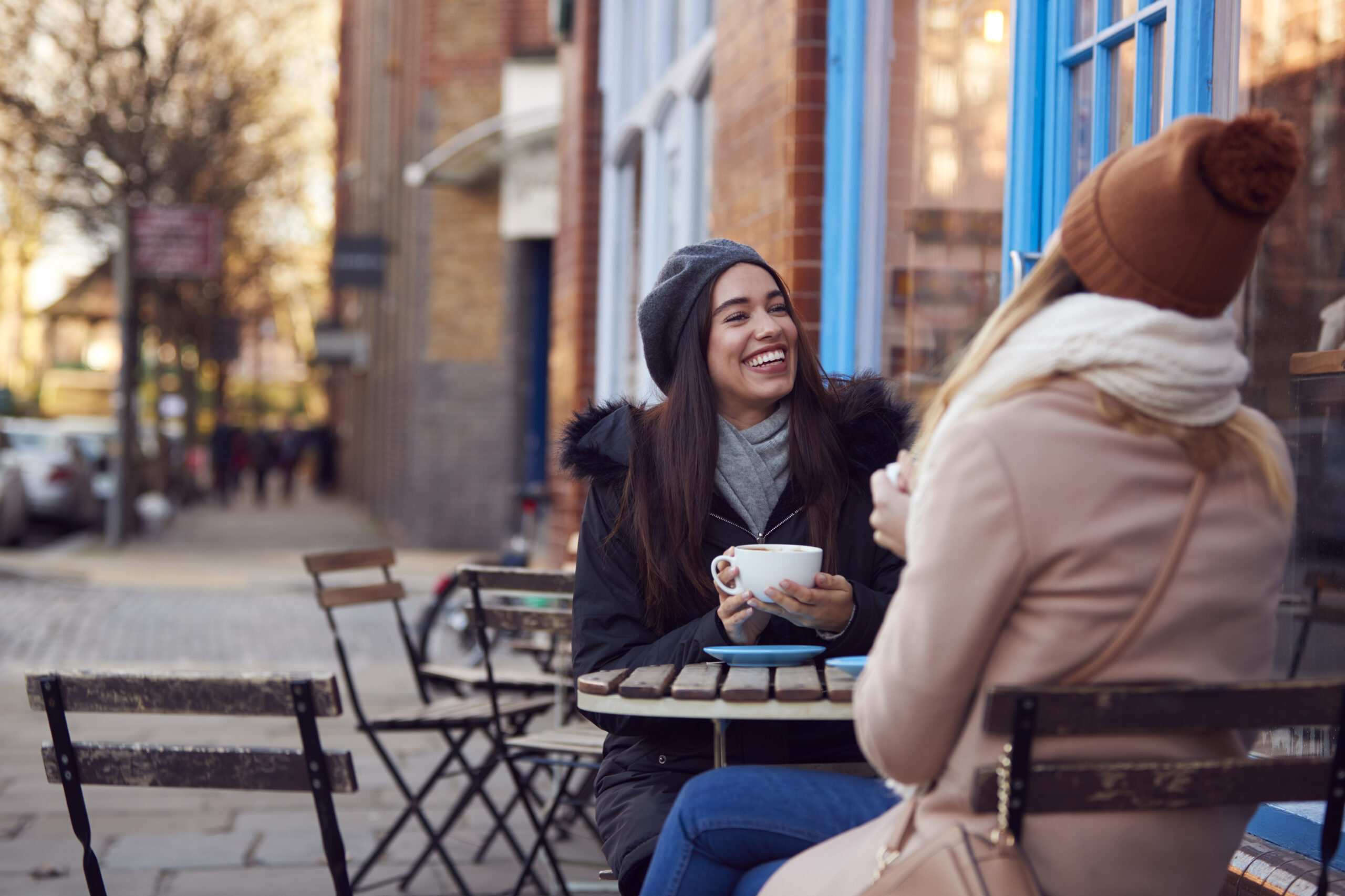 Two friends meeting and talking outside a coffee shop.