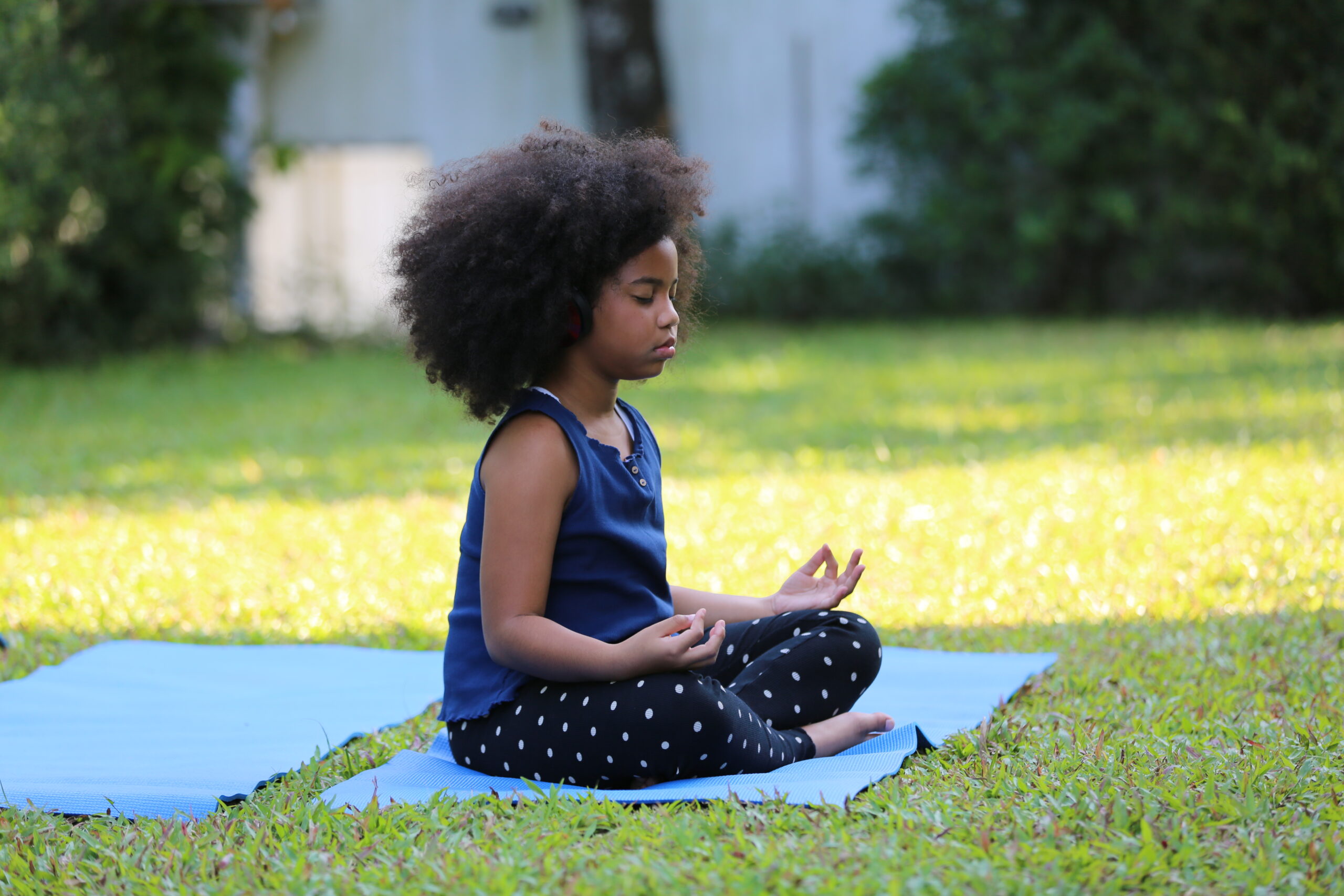 A child meditating outdoors on a yoga mat