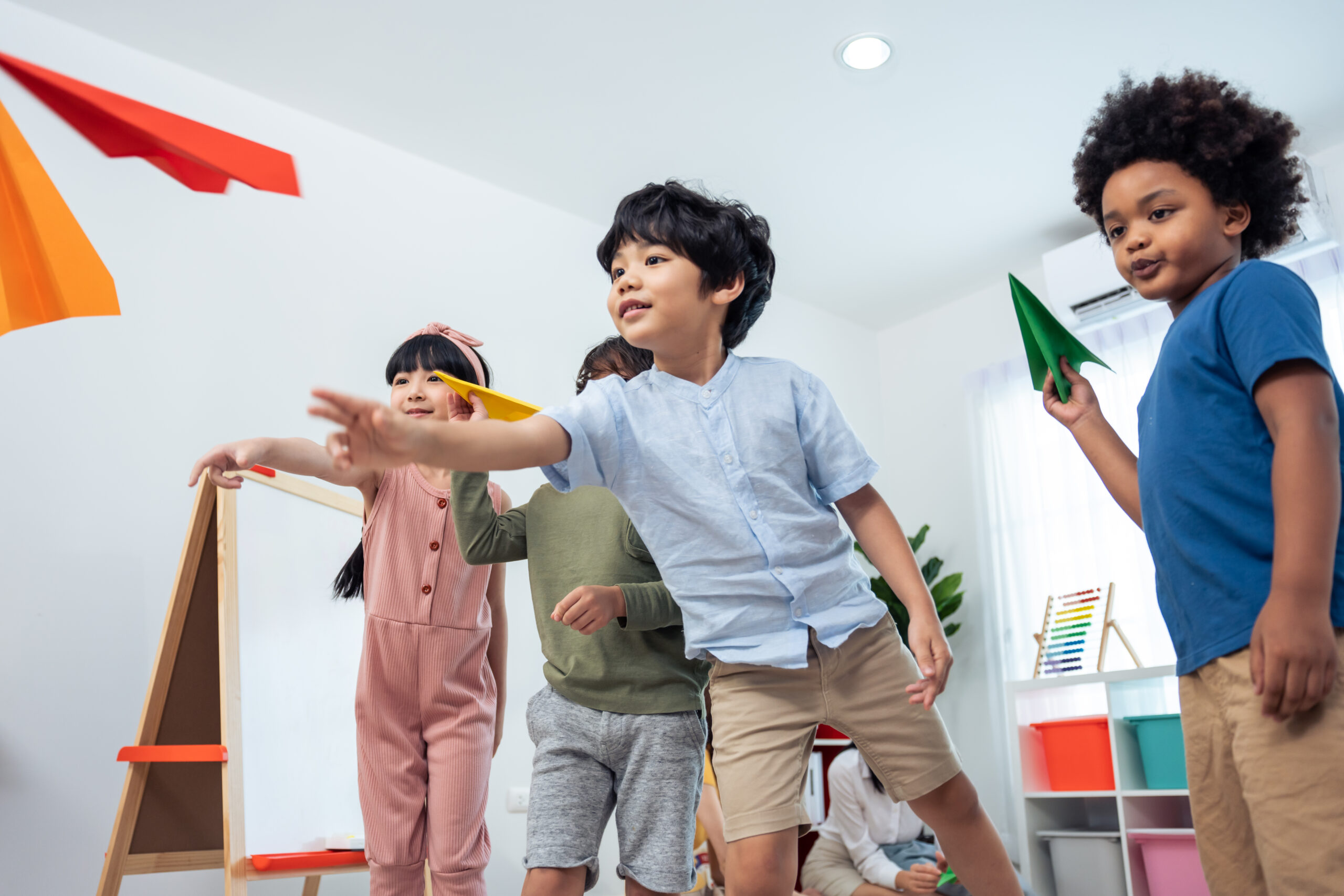 Children launching colourful paper aeroplanes indoors