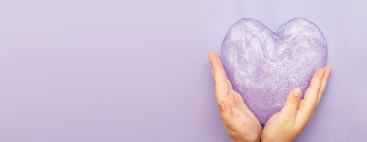 Hands holding lavender sparkling slime shaped into a heart