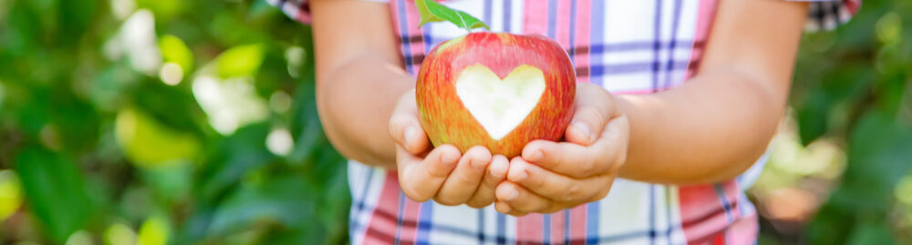 A young person outdoors holding an apple with a heart carved into it